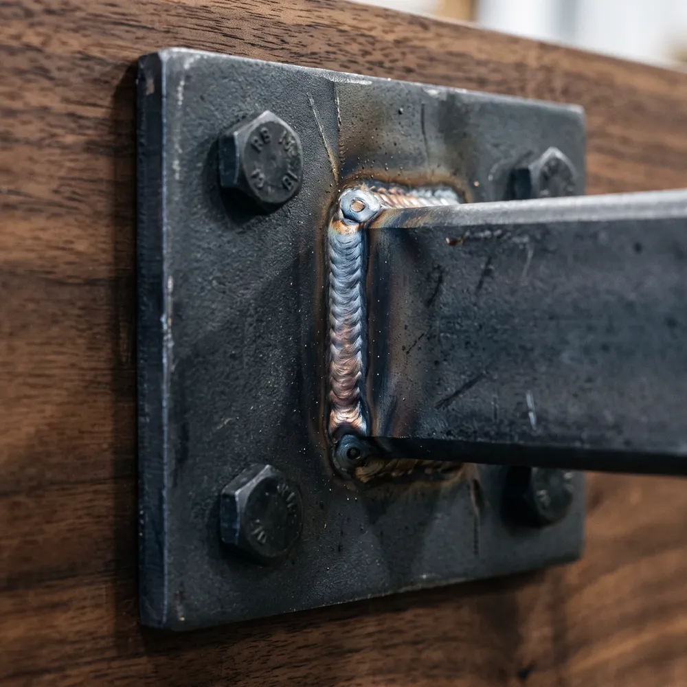 TIG weld bead on a steel mounting plate bolted to walnut